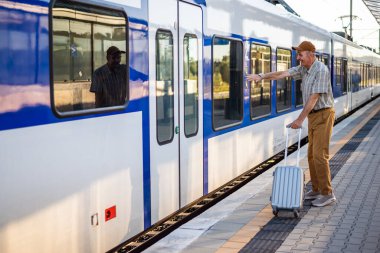 Senior man is standing at railway station. He missed the train departure and holding his head in disbelief. Senior people traveling.