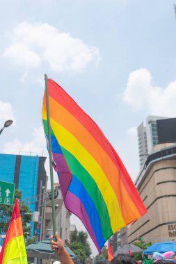 Flags lgbtttiq + dalga havada bulutlu ve güneşli bir gökyüzü ile tanınmayan insanlar,