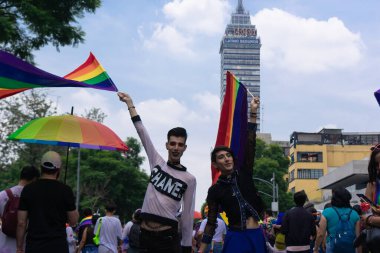 Mexico City, 25 Haziran 2022. Eşcinsel yürüyüşü sırasında el ele tutuşan katılımcılar lgbt bayrağı sallıyor. Latin Amerika Kulesi 'nin arkasında.