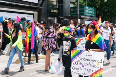 Çocuklar festivalin dönüşünde eşcinseller yürüyüşü için tabelalarla yürüyecekler. Arka planda daha fazla lgbt bayraklı odaklanmamış insanlar.