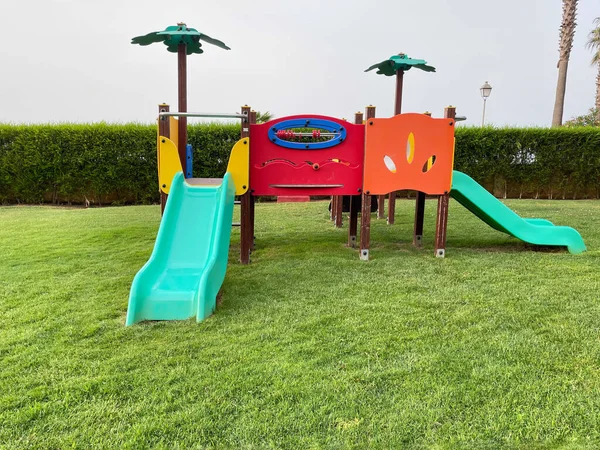 Parktaki çocuklar için renkli bir oyun alanı. Kaydırak ve palmiye ağaçları var.
