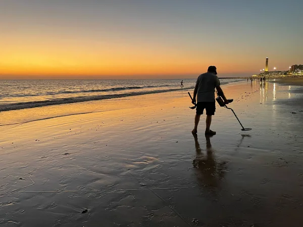 Sunset with man with metal detector on sandy beach 