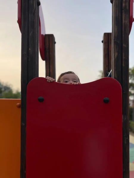 Toddler peeking into red outdoor playground