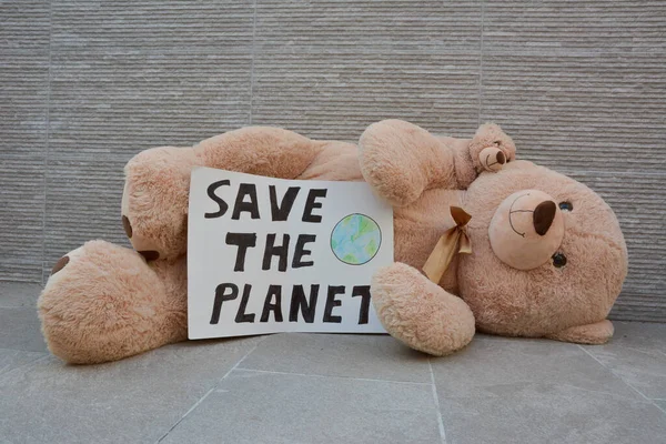 Giant teddy bear lying on the ground with save the planet poster