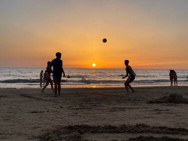 Sahilde futbol oynayan, arka planda günbatımı olan genç insanların silueti..