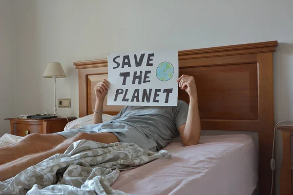 Person lying in bed holding a poster with the words save the planet