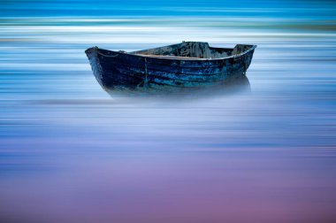 Issız eski bir tekne, dingin, sisli sularda süzülür. Canlı, bulanık bir arka plan, maviler ve morlarla..