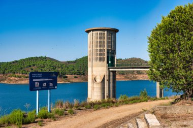 Alentejo Portekiz. 04 Ağustos 2024 Beton su kulesi ve yürüyüş yolu açık mavi gökyüzü altındaki tepelerle çevrili bir göl, Alentejo Portekiz 'deki Santa Clara barajı.