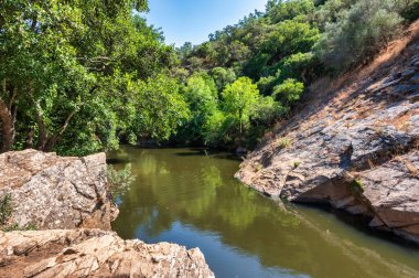 Bereketli yeşillik ve kayalık arazi ile çevrili sakin bir nehir, doğa ve seyahat kavramları için mükemmel, Pego das Pias Alentejo Portekiz 'de güzel bir arazi.