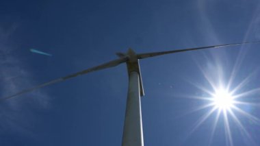 Yenilenebilir enerjiyi sembolize eden parlak mavi gökyüzüne karşı modern bir rüzgar türbininin alçak açılı görüntüsü