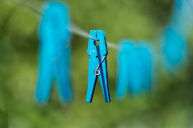 Çamaşır ipinde asılı mavi bir mandalın yakın plan görüntüsü, açık alanda bulanık yeşil bir arka plan..