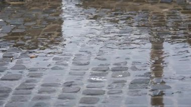 Çamurlu bir caddeye yağmur yağıyor, kasvetli gökyüzünün altında dalgalanan su birikintileri ve yansımalar yaratıyor..