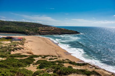 Ericeira, Portekiz 'deki Foz do Lizandro sahili, güneşli bir günde altın kum, dalga ve kıyı manzarası..