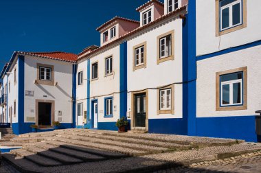 Ericeira, Portekiz 'in sakin bir caddesinde, açık mavi gökyüzünün altında taş basamakları olan renkli geleneksel evler..