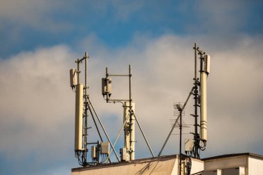 Çağdaş hücre antenleri ve radyo iletişim ekipmanları bulutlu bir gökyüzüne karşı çatıda..
