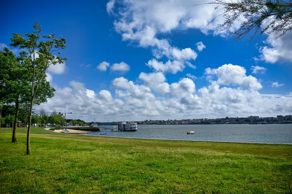 Portekiz, Seixal 'deki çimenli nehir parkı. Ağaçlar, tekneler Tejo Nehri' nde. Ve bahar günü bulutlarla dolu parlak bir gökyüzü..