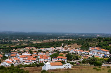 Santiago do Cacem, Alentejo, Portekiz 'in havadan görünüşü, beyaz evler, turuncu çatılar, kilise ve kırsal alan açık mavi gökyüzü altında..