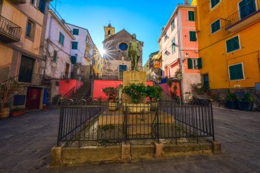 Renkli evleri olan Corniglia Largo Taragio 'nun ana meydanının manzarası, İtalya' nın Liguria bölgesindeki Cinque Terre Ulusal Parkı 'nın arka planındaki Aziz Catherine kilisesinin anıtı.