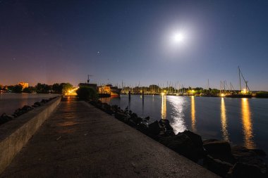 Macaristan 'daki Balaton Gölü, gece manzaralı. Yatlı manzara, deniz feneri, yıldızlı ve aylı koyu mavi gökyüzü, yansımalı sakin su, arka planda açık hava yolculuğu