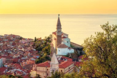 Piran Eski Kasabası, Slovenya, manzaralı şehir manzarası. Ortaçağ mimarisinin St. George, Adriyatik Denizi Kilisesi ve gökyüzü manzarası Eski Şehir Duvarları 'ndan gün batımı ışığı, dış seyahat arka planı