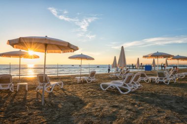 Güzel kumlu plaj aksesuarları, durgun deniz, mavi gökyüzü, bulutlar ve yükselen güneş yumuşak sabah ışığında, manzaralı deniz manzarası, yaz tatili ve seyahat konsepti, Larnaca, Kıbrıs