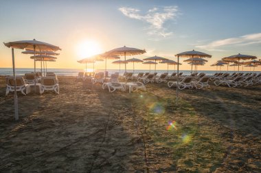 Güzel kumlu plaj aksesuarları, durgun deniz, mavi gökyüzü, bulutlar ve yükselen güneş yumuşak sabah ışığında, manzaralı deniz manzarası, yaz tatili ve seyahat konsepti, Larnaca, Kıbrıs