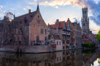 Belçika 'nın Rozenhoedkaai (Tespih İskelesi) kentinden Bruges' ün en popüler manzarası. Ortaçağ tarihi binaları ve gün batımında Dijver kanalı boyunca çan kulesiyle manzaralı bir şehir.