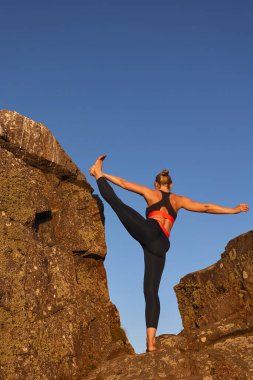 Uçurumun kayaları arasında yoga yapan bir kadının telif uzayı ile dikey görüntüsü