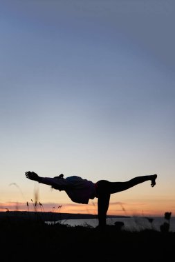 Güzel bir kadın silueti. Gün doğumunda yoga yapıyor. Tanınmayan bir yüz ve reklam için büyük bir fotokopi alanı var.