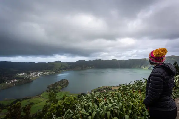 stock image A stunning view of Sete Cidades Lake on Sao Miguel Island, Azores. The lake is framed by lush green hills under a dramatic cloudy sky, with patches of sunlight breaking through. Small settlements dot the shoreline, enhancing the charm of this picture