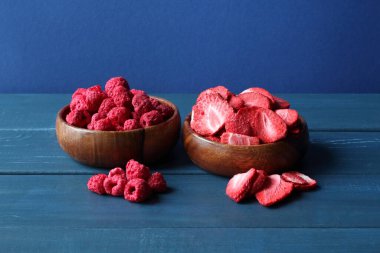 Kurutulmuş ahududu ve dilimlenmiş çilek ahşap kaselerde mavi ahşap masada duruyor. - Yakın çekim. Makro