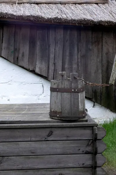 Tahta bir bina ve beyaz bir duvar ile kuyunun üzerinde asılı eski ahşap kova su
