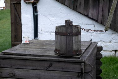 Tahta bir bina ve beyaz bir duvar ile kuyunun üzerinde asılı eski ahşap kova su