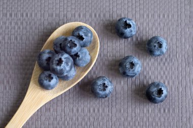 Ahşap kaşıkta organik yaban mersini, gri desenli arka plan, ön manzara. Vegan, sağlıklı yaşam tarzı, tazelik, yaz, hasat, doğal gıda kavramı