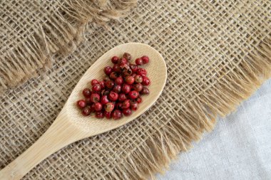 Ahşap kaşıkta kırmızı ya da pembe biber, gri desenli keten arka plan manzarası.