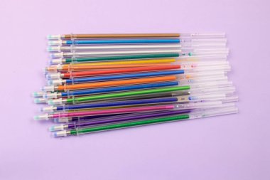 Mor arkaplan kırtasiyesinin üst görünümünde çok renkli tükenmez kalemler ve mürekkep dolguları