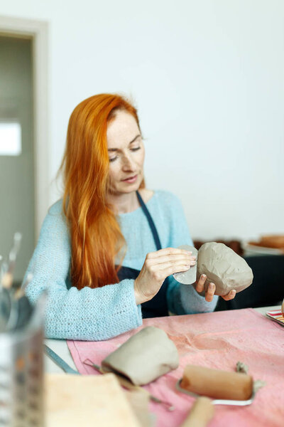 Pottery studio, artisan business,red hair female potter holding ceramic bowl ready for firing in a kiln.