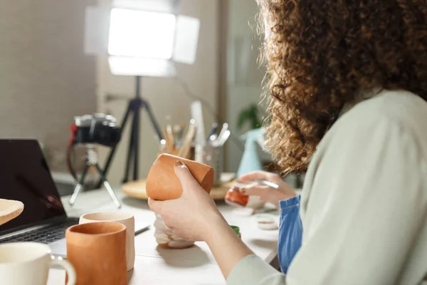 Females potter in blue apron making a vlog, recording online course, clay master class,lessons in her studion with earthenware.Using led lamp,studio equipment.