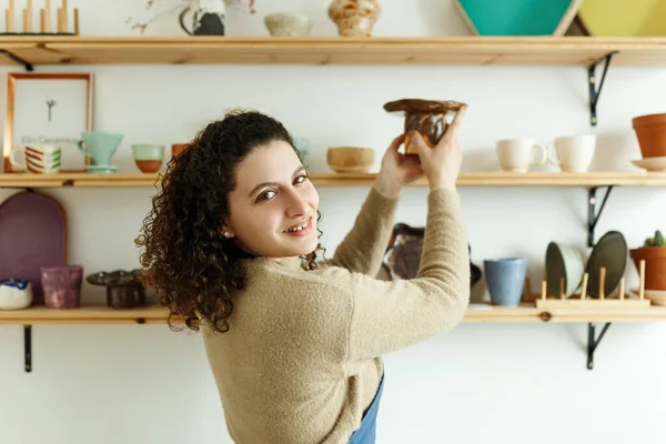 stock image Happy young ceramist looking away thoughtfully while taking stock. Creative businesswoman managing a store with handmade ceramic products. Female entrepreneur running a successful small business.