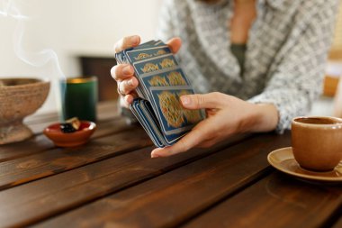 Mumun yanındaki masada tarot kartlarıyla falcı. Masaya sihirli otlar ve palo santo aroma çubukları serpiştirilmiş tarot kartları. Tahmin konsepti