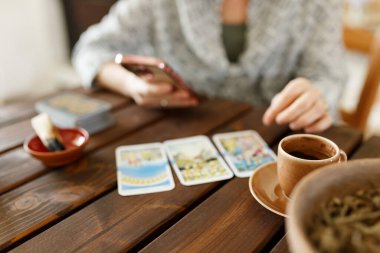 Mumun yanındaki masada tarot kartlarıyla falcı. Masaya sihirli otlar ve palo santo aroma çubukları serpiştirilmiş tarot kartları. Tahmin konsepti