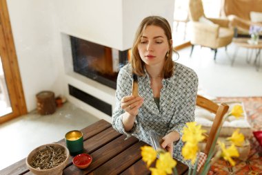 Kadın elleri Palo Santo 'yu yakmadan önce, masada mumlar ve yeşil bitkilerle. Leke dumanı acıyı ve stresi tedavi eder. Negatif enerjiyi ve meditasyon çubuğunu temizler...