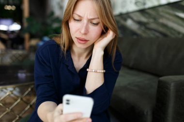Genç kadın üzgün, kötü haber e-postaları okuyor, eski erkek arkadaşından mesajını akıllı telefondan kesiyor oturma odasındaki kanepede tek başına oturuyor. Üzgün mutsuz kadın cep telefonunda kalp kırıcı mesajlar atıyor..