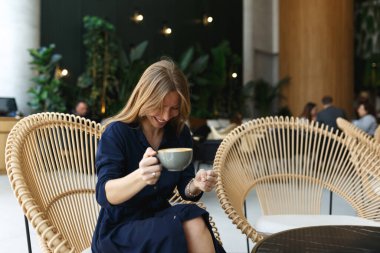 Evde kahve içen neşeli genç bir kadının portresi. Gülümseyen güzel kız sıcak içecek içiyor. İçi yeşil, mavi elbiseli heyecanlı bir kadın, cappuccino kokuyor..