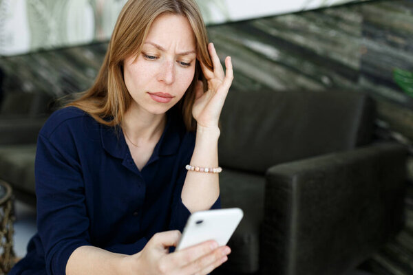 Young woman sad, reading bad news email, break up message from ex-boyfriend on smartphone sitting lonely on couch in living room. Depressed unhappy female desperate of heartbreak sms on mobile phone.
