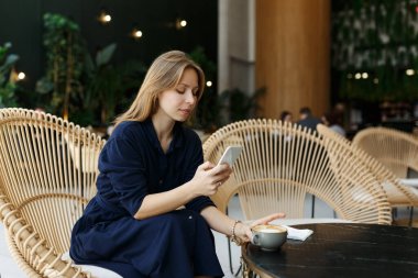 Cafe 'de cep telefonuyla bir fincan aromatik kahveyle sohbet eden hoş bir kadın. Çekici bir genç bayan cep telefonuyla içeride pencerenin yanında sohbet ediyor. Gülümsüyor 