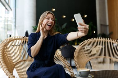 Moda kadın blogcusu bir kafede elinde telefonla oturmuş bir mesaj okuyor, mobil iletişim ve internet seyahati, video görüşmesi, serbest çalışma, dişleriyle gülümseme.. 