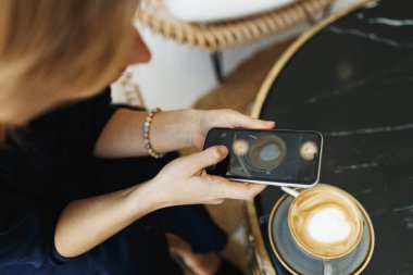 Kadın akıllı telefonuyla kahve fotografı çekiyor. Üst görünüm