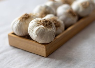 Yakın plan, beyaz sarımsak beyaz arka planda, kare ahşap kabın üzerinde.