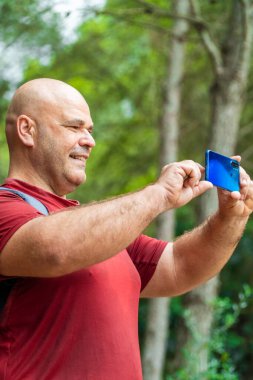  Terli, iri yarı, erkek bir yürüyüşçü akıllı telefonuyla video kaydediyor.